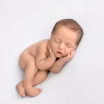 Newborn baby details boy Jeffery with dark brown hair naked asleep with his little baby hands curled around his round cheeks lying on his side with his legs crossed on white blanket newborn photographer Gainesville Florida