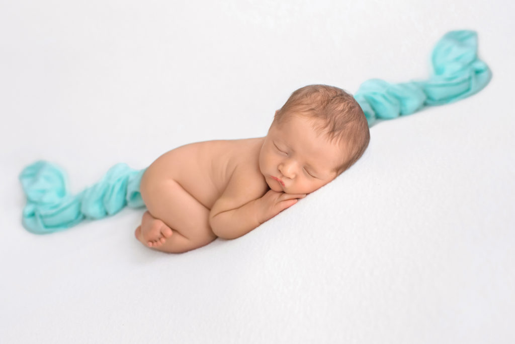 Newborn boy Jeffery naked asleep with chin resting on his hand lying on his tummy with bottom up on white blanket with mint green heart and mint accent blanket newborn photographer Gainesville Florida