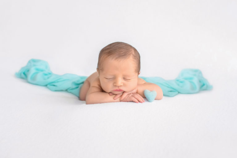 Newborn boy Jeffery asleep with chin resting on his hands lying on white blanket with mint green heart and accent blanket newborn photographer Gainesville Florida