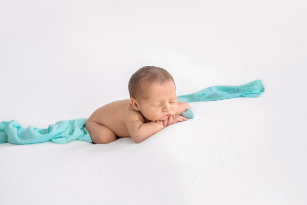 Newborn boy Jeffery asleep with chin resting on his hands lying on white blanket with mint green heart and accent blanket side view newborn photographer Gainesville Florida