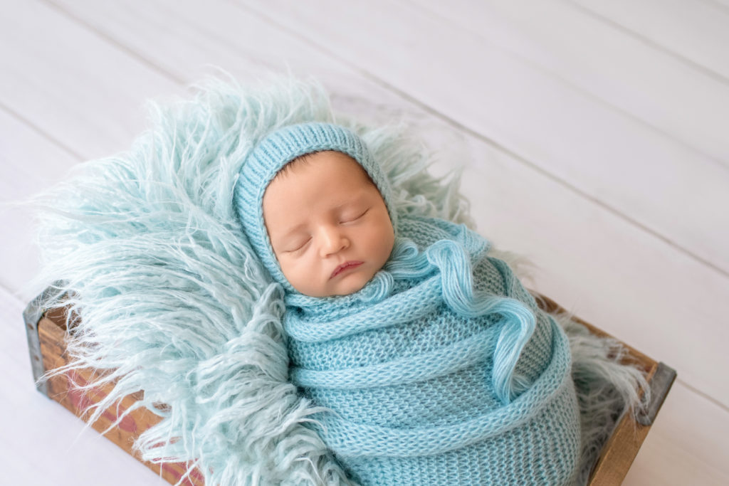 handsome Gainesville newborn pictures Jeffery in blue knit wrap and matching blue bonnet posed in blue fur stuffed Pepsi crate