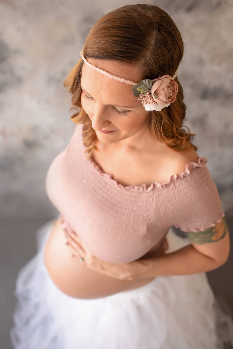 Beautiful pregnant mom to be in white tulle tutu posed with close up hands on bare belly against pastel blue grey rose painted backdrop Gainesville maternity photography