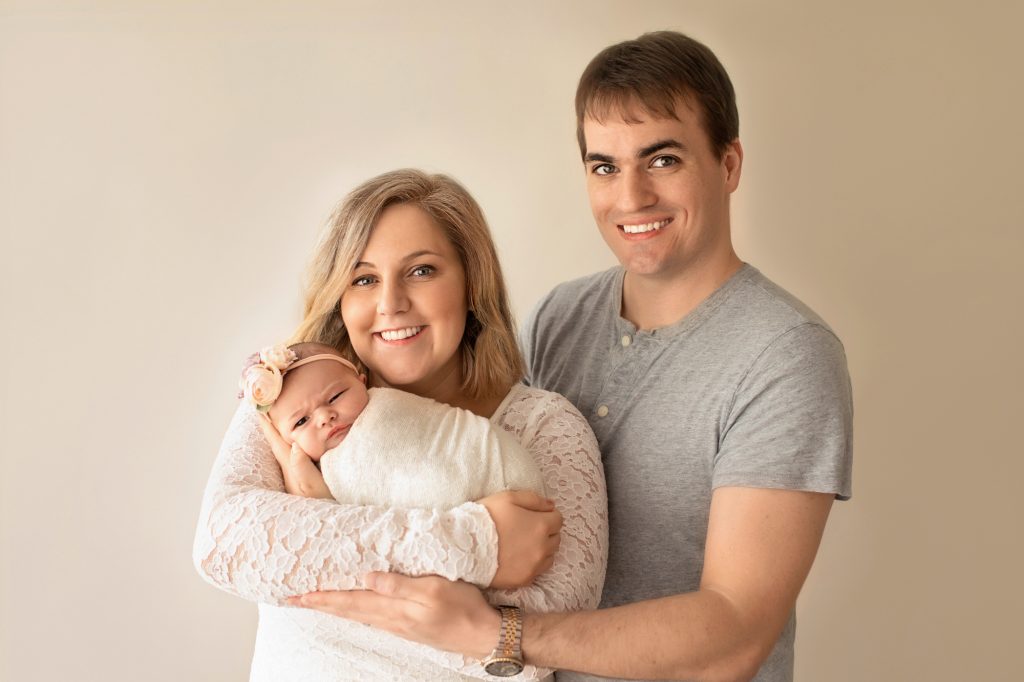 Gainesville Newborn moments Mom and Dad holding their tiny newborn baby girl Chloe in cream wrap and floral headband first family portrait Gainesville Florida newborn photography