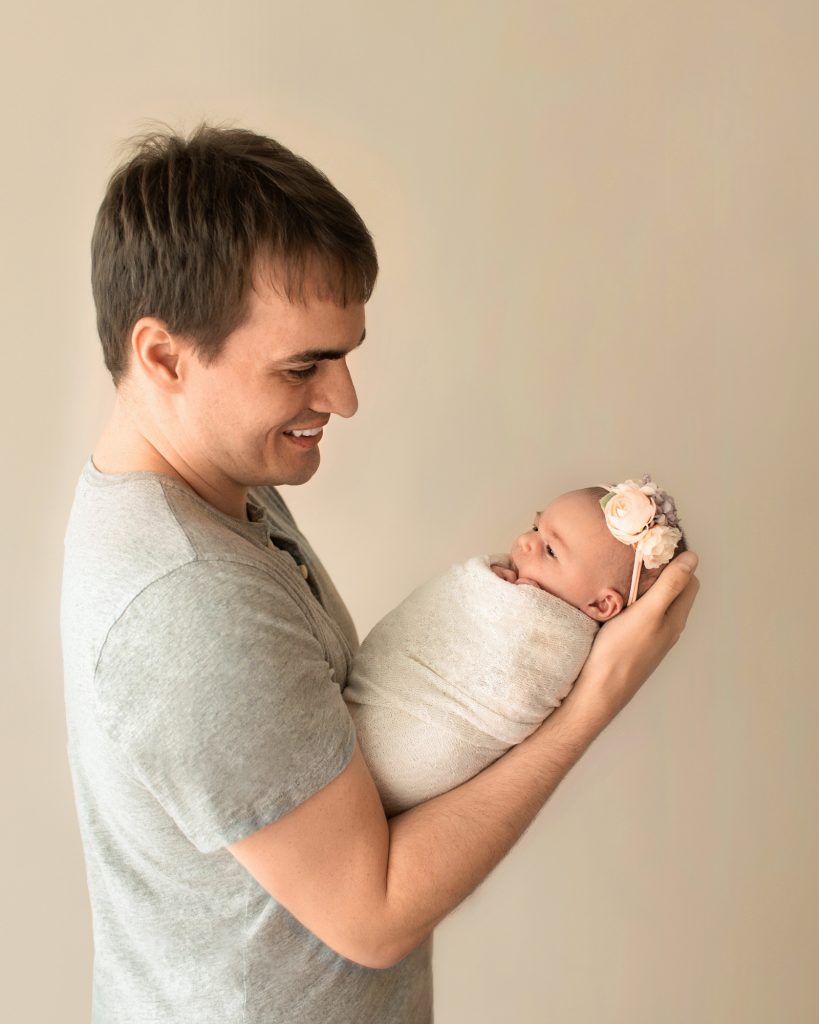 Gainesville Newborn moments Proud dad Ben looking with wonder as he holds his tiny newborn baby girl Chloe with eyes wide open in cream wrap and floral headband