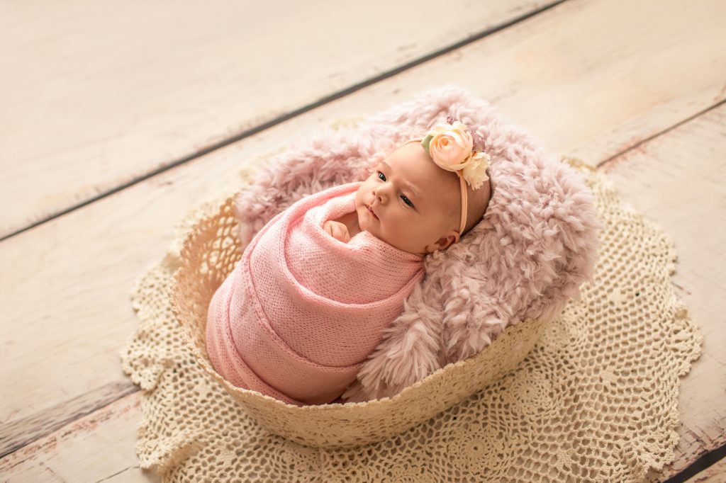 Gainesville Newborn moments newborn baby girl swaddled in pink knit wrap and floral headband posed in pink fur stuffed lace basket with lace accents Gainesville Florida newborn photography