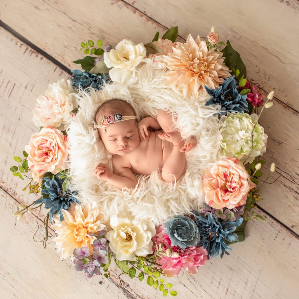 Gainesville Newborn moments newborn baby girl posed naked with delicate floral headband against white fur surrounded by dusty blue pink and ivory flowers Gainesville Florida newborn photography