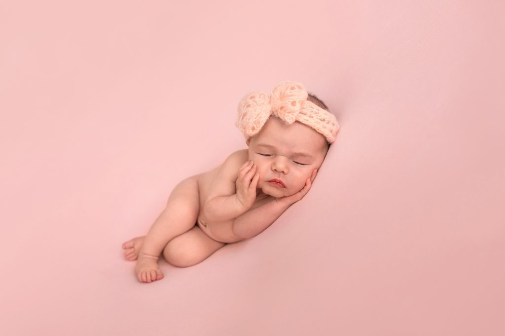 Gainesville Newborn moments newborn baby girl posed naked with pink handmade knit headband newborn baby hands cupping her cheeks posed on her side on dusty pink blanket Gainesville Florida newborn photography