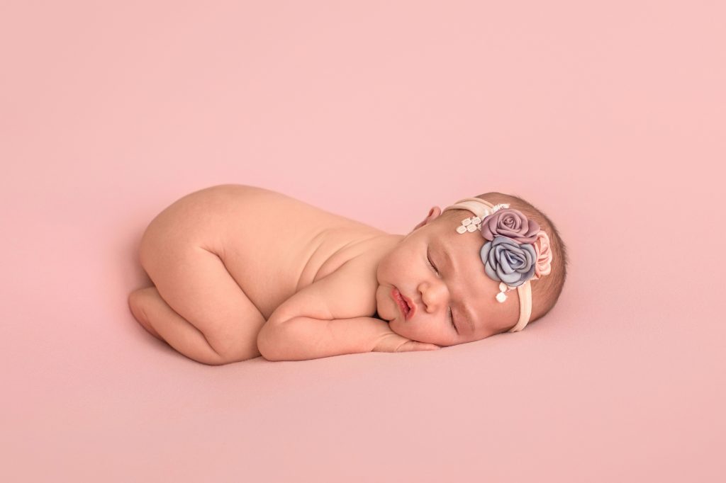 Gainesville Newborn moments newborn baby girl posed naked with dusty blue pink lavender floral headband newborn baby posed on belly with bottom up resting head on her hands lying on dusty pink blanket Gainesville Florida newborn photography