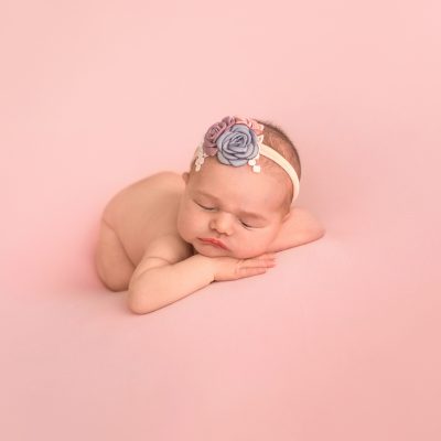 Gainesville Newborn moments baby girl posed naked with dusty blue pink lavender floral headband newborn baby posed on belly with bottom up resting chin upright on her hands lying on dusty pink blanket Gainesville Florida newborn photography