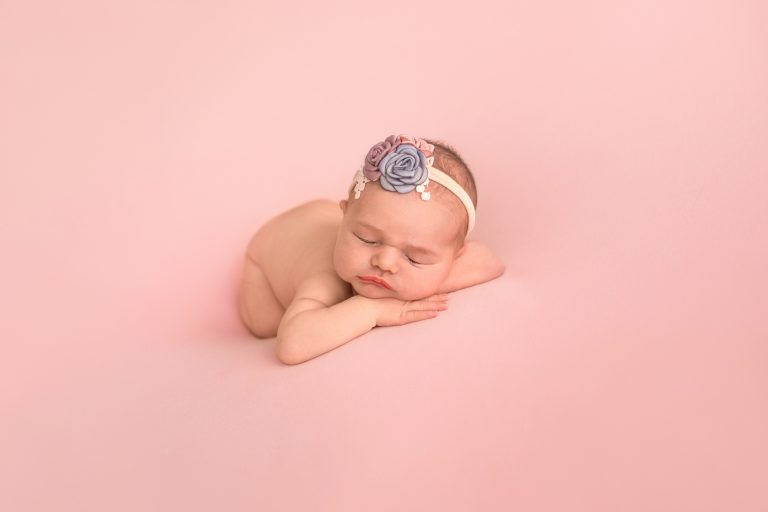 Gainesville Newborn moments baby girl posed naked with dusty blue pink lavender floral headband newborn baby posed on belly with bottom up resting chin upright on her hands lying on dusty pink blanket Gainesville Florida newborn photography