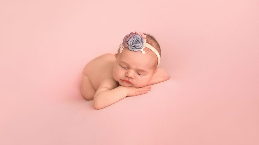 Gainesville Newborn moments baby girl posed naked with dusty blue pink lavender floral headband newborn baby posed on belly with bottom up resting chin upright on her hands lying on dusty pink blanket Gainesville Florida newborn photography