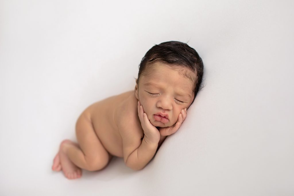 newborn photoshoot Christian posed naked on white blanket with tiny hands cupping little newborn cheeks head resting on his hand lots of dark brown hair Gainesville FL newborn photography