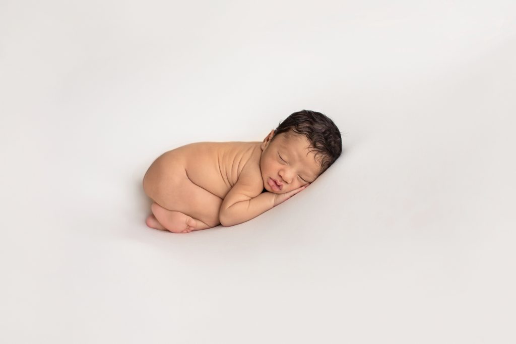 newborn photoshoot Christian posed naked on belly on white blanket with head resting on his hands bottoms up lots of dark brown hair photo from the side Gainesville FL newborn photography