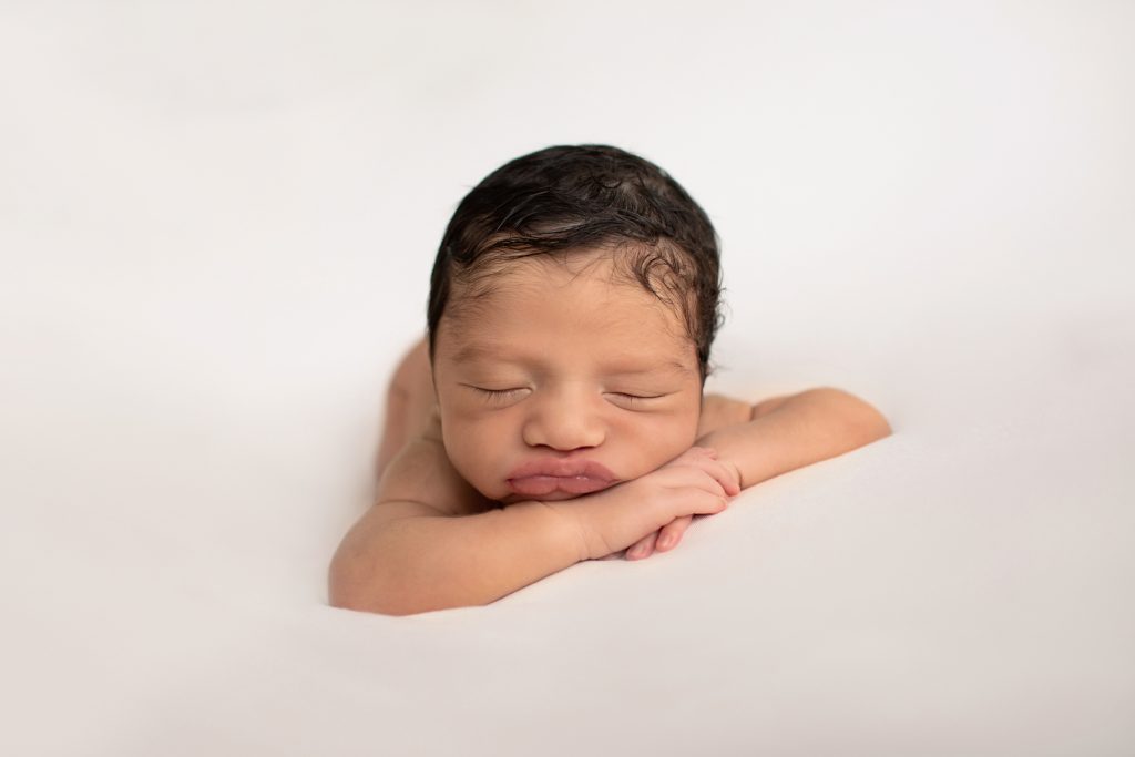 newborn photoshoot Christian posed naked on belly on white blanket with hands folded chin propped on hands head upright lots of dark brown hair Gainesville FL newborn photography