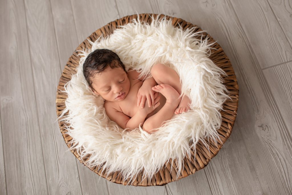 newborn boy Christian posed naked in fur stuffed brown basket on grey wood floor Gainesville Fl newborn picture