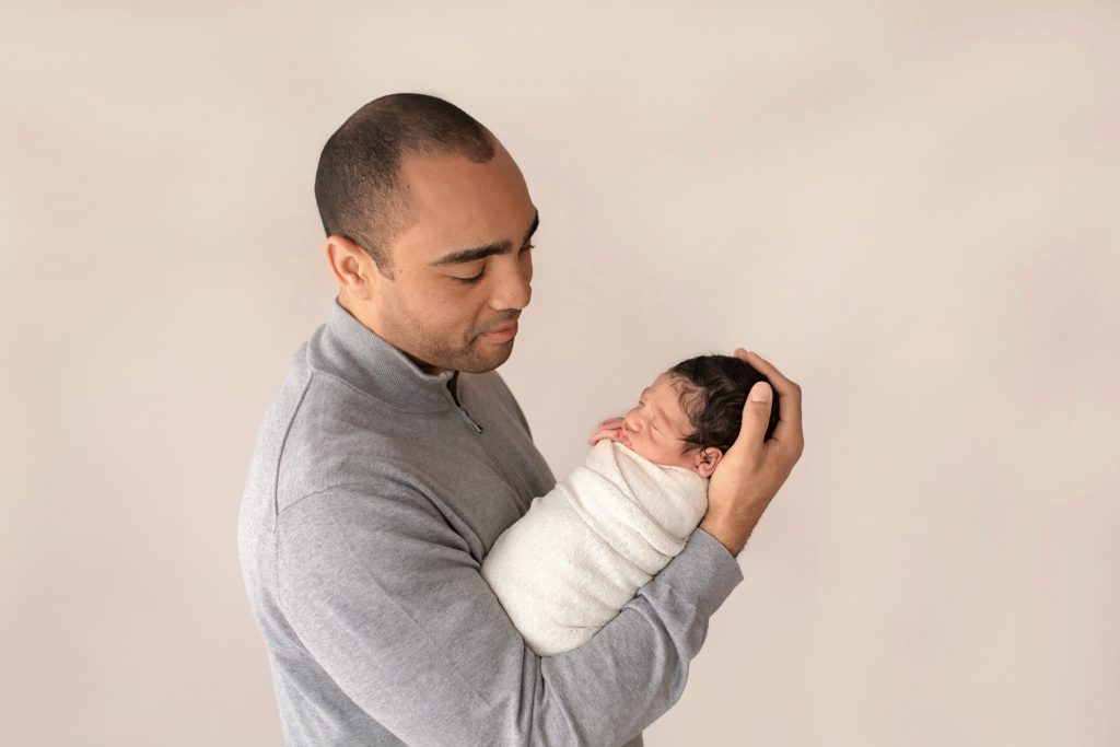 handsome dad profile photo holding and gazing into eyes of newborn Christian bundled in cream knit wrap Gainesville Fl newborn picture