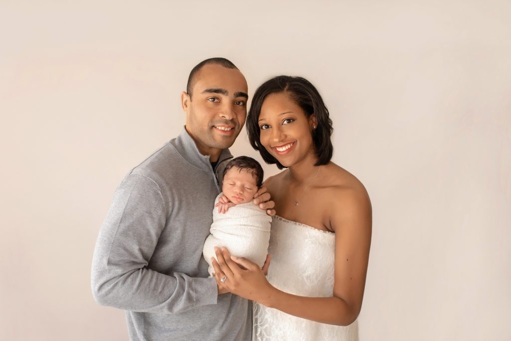 newborn photoshoot Christian bundled in cream knit blanket posed in arms of gorgeous mom wrapped in ivory lace and handsome dad smiling at camera with hearts full of joy Gainesville Fl newborn picture