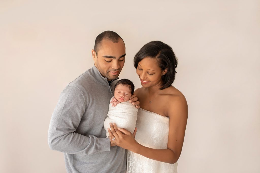 newborn photoshoot boy Christian bundled in cream knit blanket posed in arms of gorgeous mom wrapped in ivory lace and handsome dad gazed lovingly at baby Gainesville Fl newborn picture