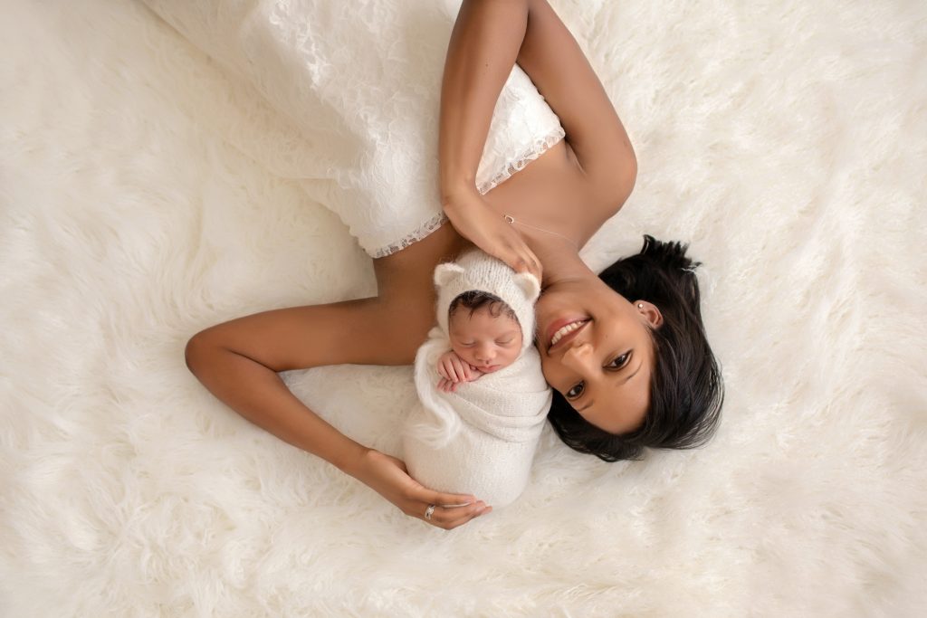 newborn photoshoot Christian bundled in cream knit blanket with matching bear bonnet poses with gorgeous mom in ivory lace on cream fur Gainesville Fl newborn picture