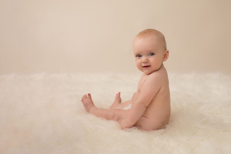 six month naked baby Rachel with eyes locked to camera chin to shoulder like a little baby model posed beautifully on white fur sitting up smiling family heirloom photos