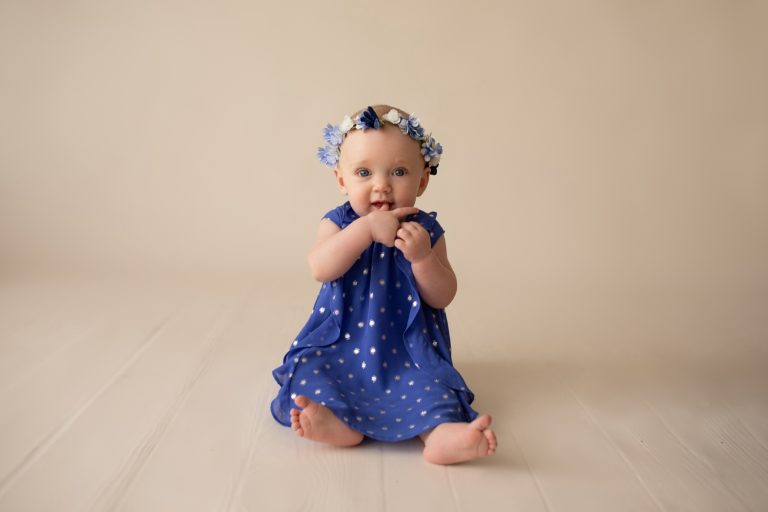 beautiful baby photos 6 month girl family heirloom photos wears blue polka dot dress and floral crown hands in mouth