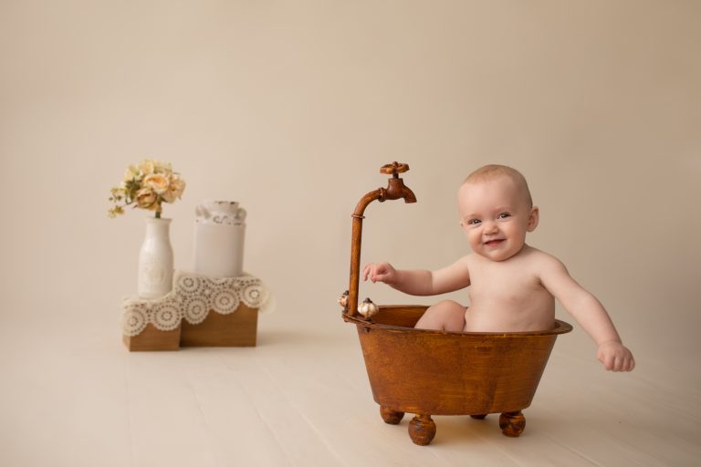 six month naked baby Rachel smiles with personality sitting in brown old fashioned tub with big smiles