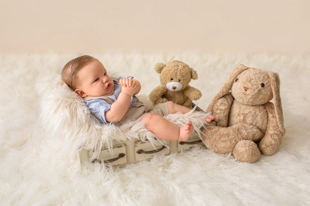 Baby in khaki shorts button up collared shirt suspenders with favorite teddy bear looking at mom