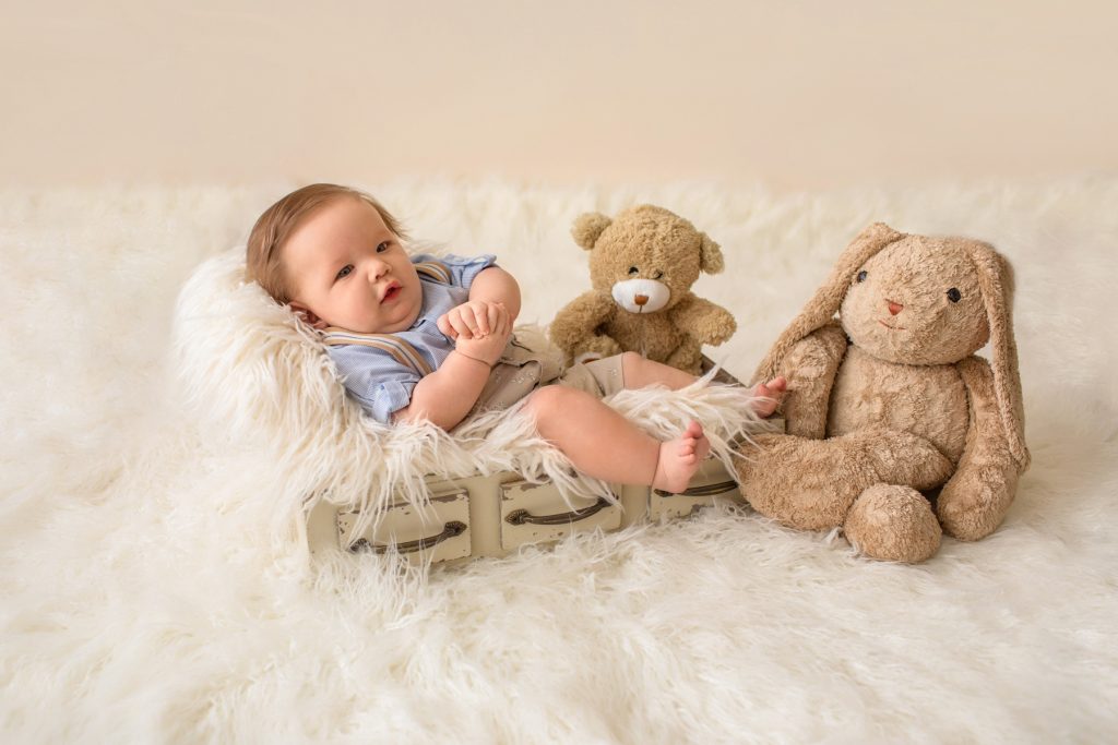 Baby in khaki shorts button up collared shirt suspenders holding his hands with favorite teddy bear