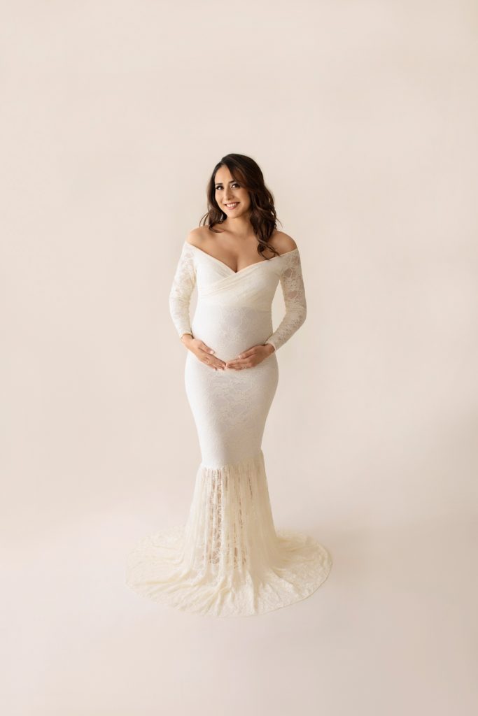 Gorgeous pregnant mom dressed in long sleeved ivory lace mermaid maternity gown smling at camara