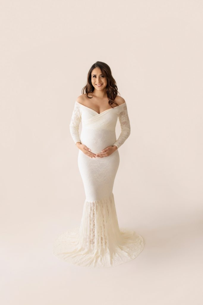 Maternity pictures gorgeous pregnant mom dressed in long sleeved ivory lace mermaid maternity gown smiling straight at camera