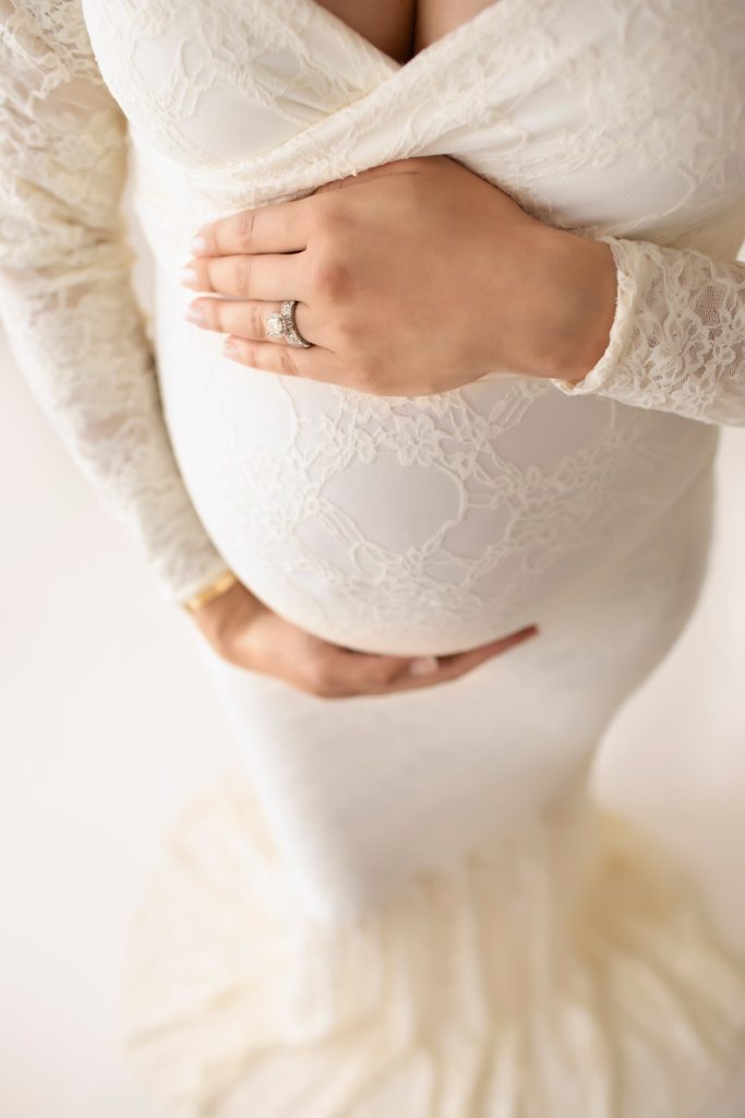 Gorgeous pregnant mom dressed in long sleeved ivory lace mermaid maternity gown shooting down toward belly