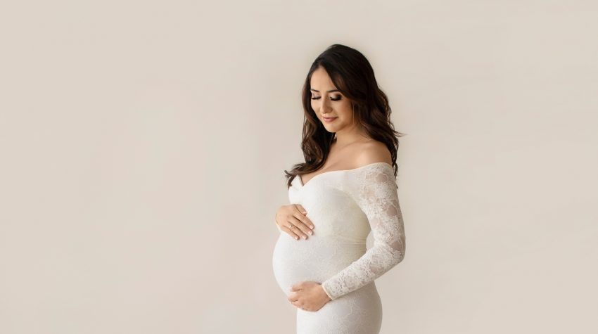 Gorgeous pregnant mom dressed in long sleeved ivory lace mermaid maternity gown proflie shot looking down at beautiful baby belly