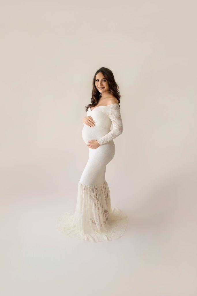 Gorgeous pregnant mom dressed in long sleeved ivory lace mermaid maternity gown smiling at camera profile shot