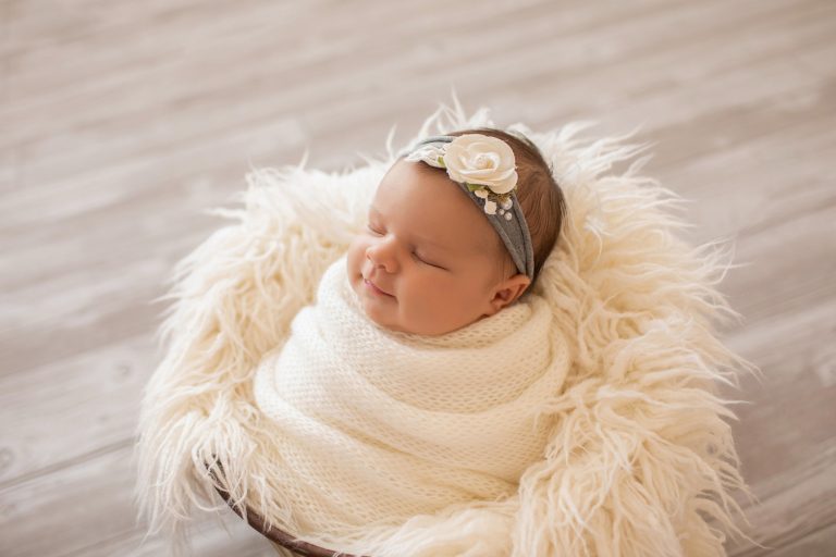 tiny baby girl Bryce swaddlied in white hand knitted blanket posed like a little potato sack in a bucket with white fur