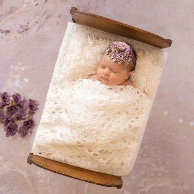 tiny baby girl Bryce sleeps under white lace blanket in baby bed with purple flowers and matching headband