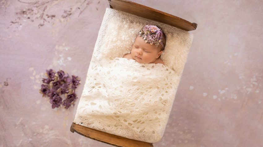 tiny baby girl Bryce sleeps under white lace blanket in baby bed with purple flowers and matching headband
