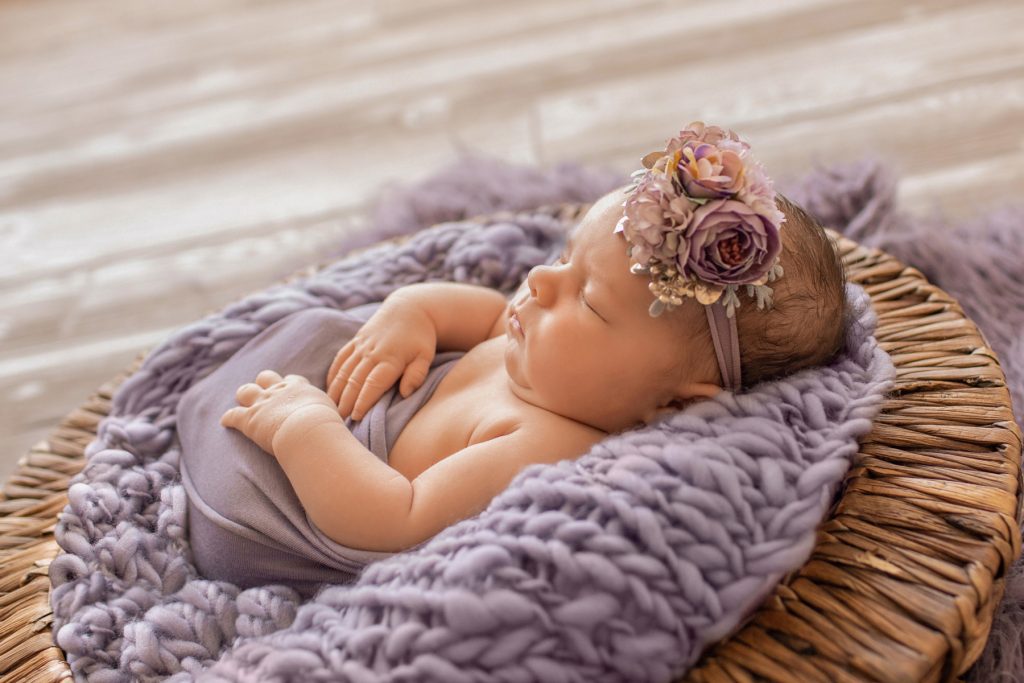 Profil newborn girl Bryce poses with purple wrap and fur in brown basket