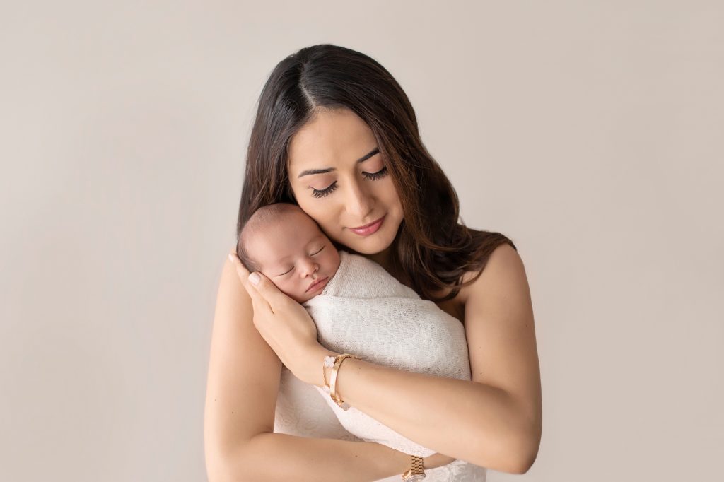 Mom wrappling newborn in arms of love bundled in cream knit blanket cuddle time