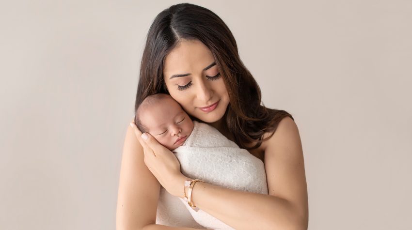 Mom wrappling newborn in arms of love bundled in cream knit blanket cuddle time