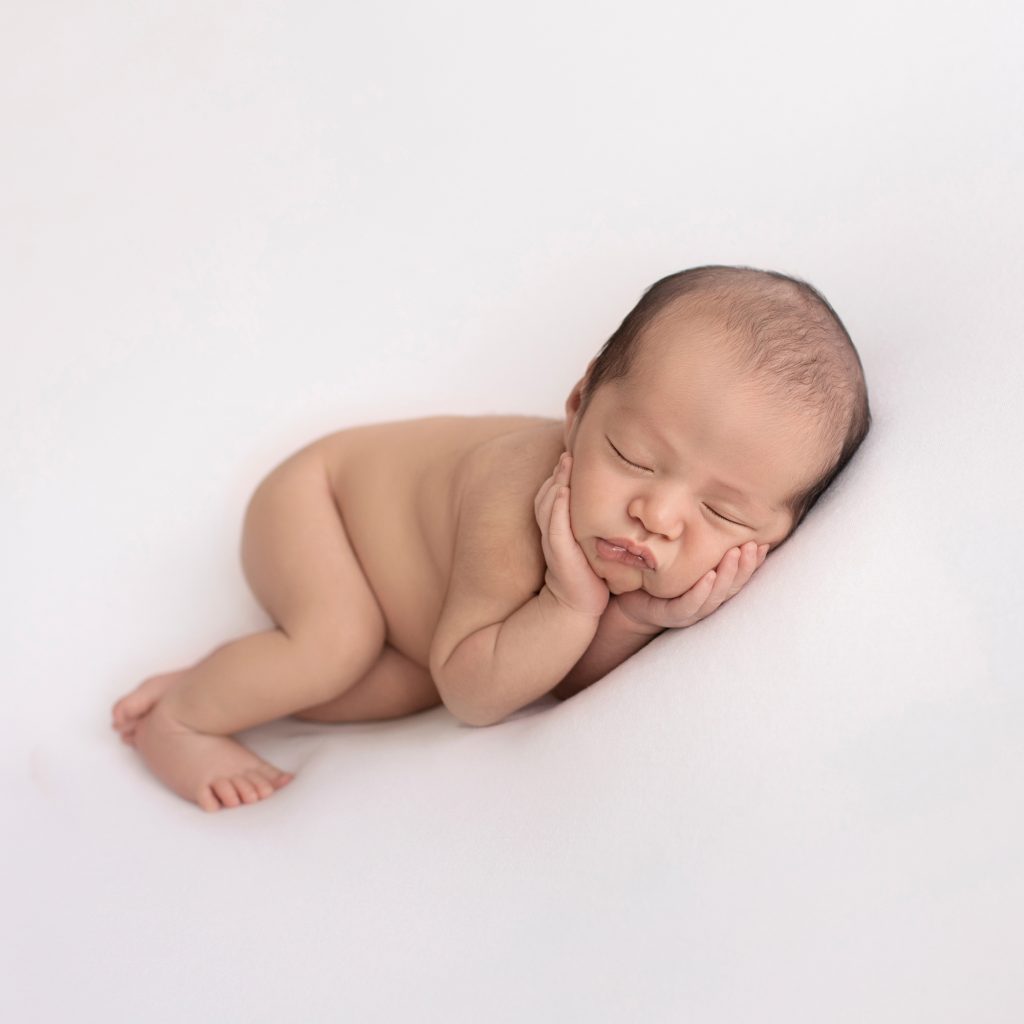naked newborn image boy posed resting on his side cupping his face adorable squishy baby cheeks