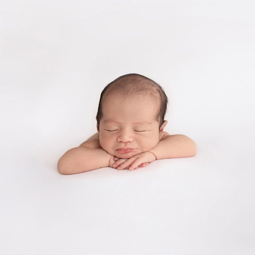 Newborn soft baby skin posed naked head resting on hands face to camera