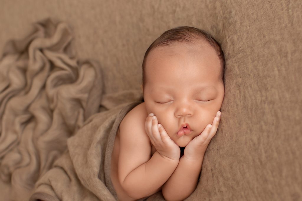 Lucas on brown blanket with baby hands cupping his beautiful baby face toward camera brown blanket rolls decorating the background