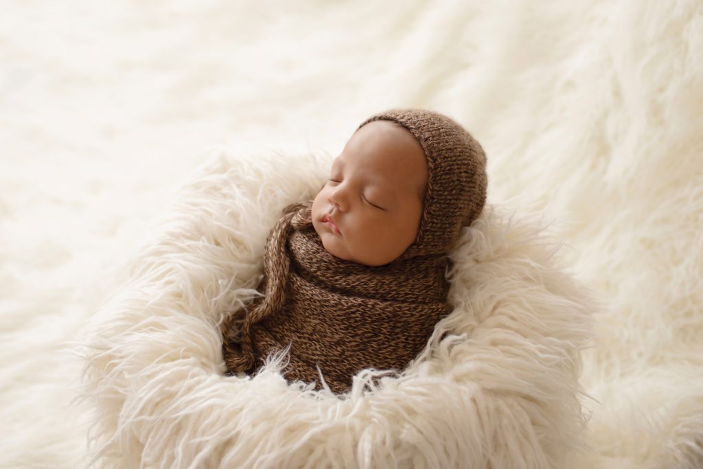 Lucas baby newborn wrapped like a brown potato sack with matching knit bonnet against back light