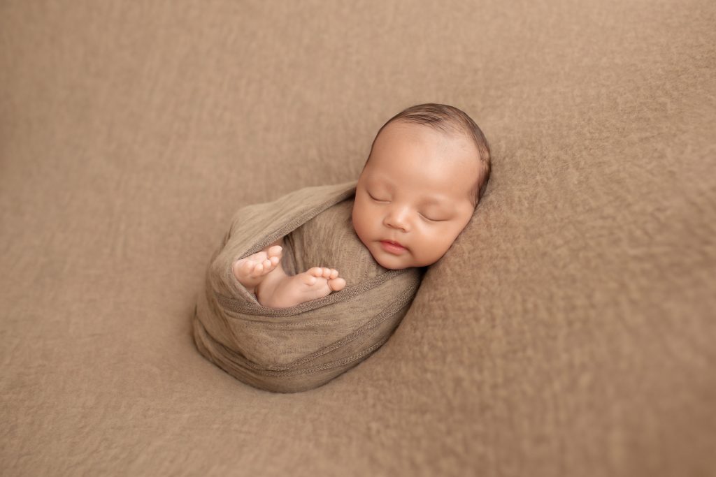 Smiling Lucas in brown swaddle with toes poking out and beautiful baby face toward camera