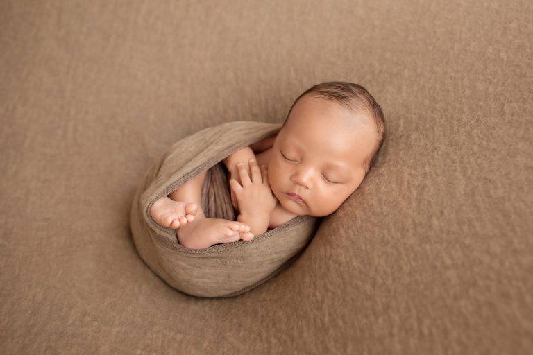 Lucas in brown swaddle with hands and toes poking out and beautiful baby face toward camera