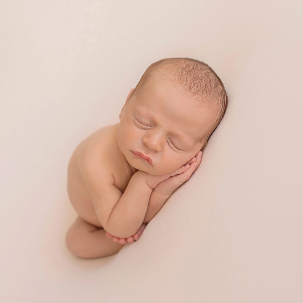 naked newborn baby sleeping with hands under cheeks and teeny tiny toes cupping elbow against white blanket