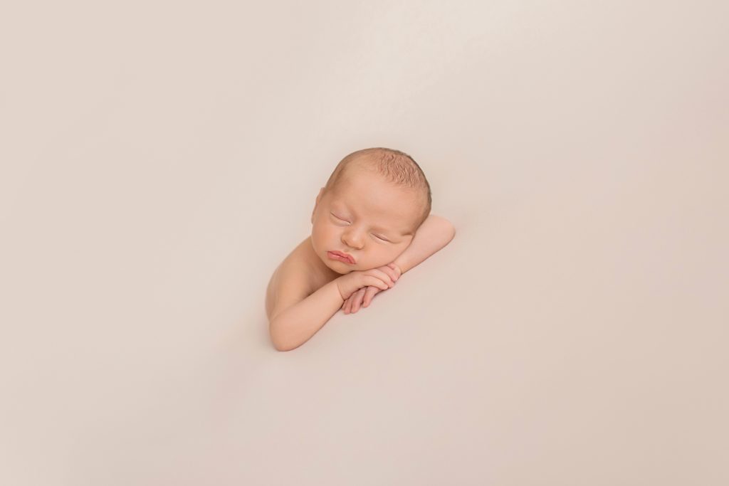 naked baby sleeping in his hands resting forward against white blanket