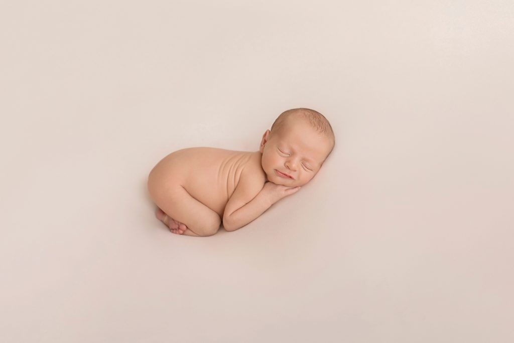 naked baby smiling sleeping with tush up and tiny hands under cheeks against white blanket