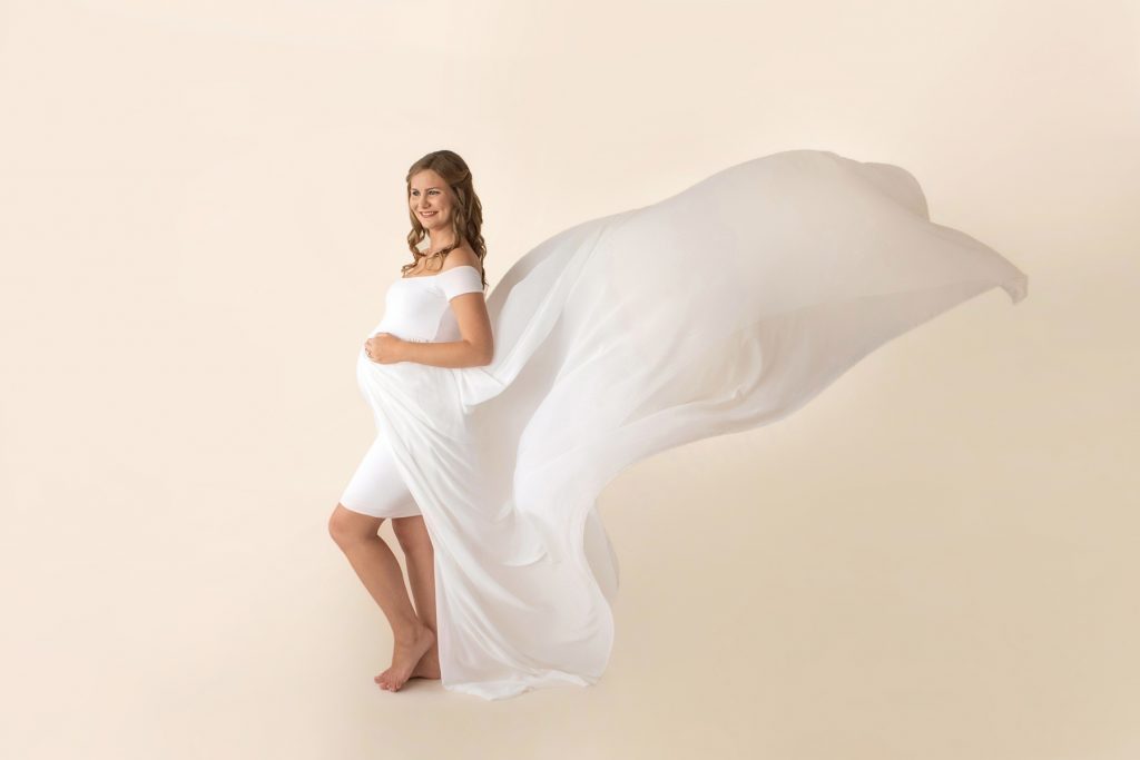 Gorgeous new mom long blond curls in white chiffon maternity gown with tossed train