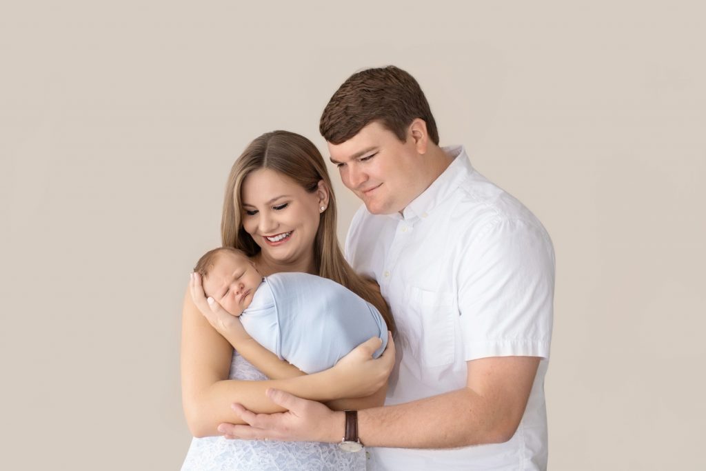 Smiling new mom and dad delighted smiling at baby boy first family portrait swaddled in pale blue
